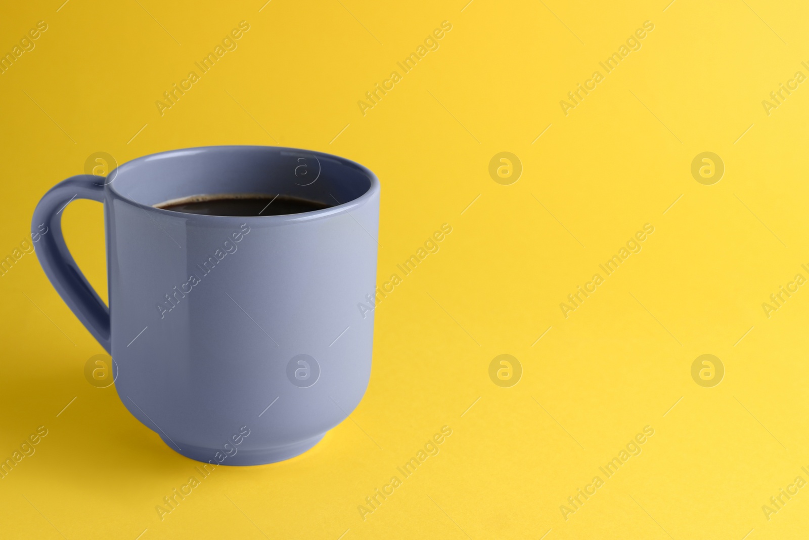 Photo of Grey mug of freshly brewed hot coffee on yellow background, space for text