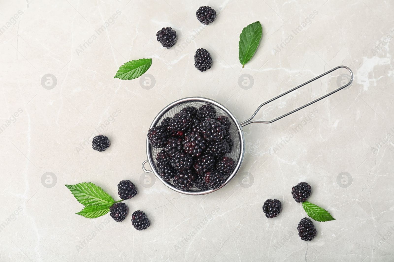 Photo of Flat lay composition with strainer of fresh blackberry and leaves on gray background