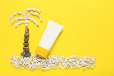 Photo of Suntan cream and palm made of marble pebbles on yellow background, flat lay. Space for text