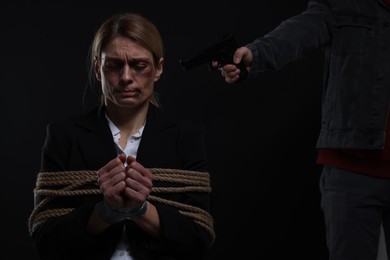 Kidnapper pointing gun at tied up woman taken as hostage on dark background