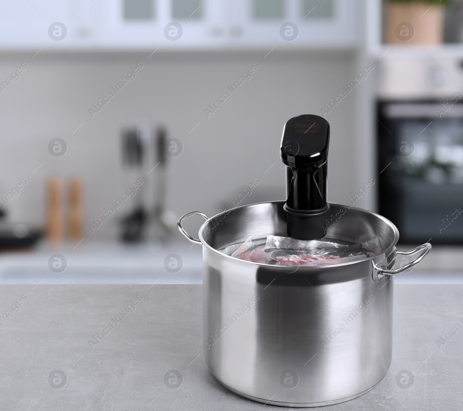 Image of Sous vide cooker and vacuum packed food products in pot on light marble table in kitchen, space for text. Thermal immersion circulator