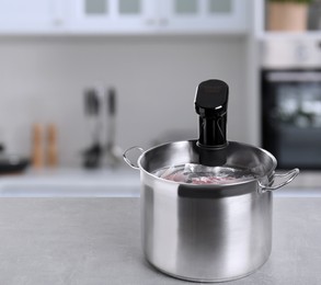 Image of Sous vide cooker and vacuum packed food products in pot on light marble table in kitchen, space for text. Thermal immersion circulator