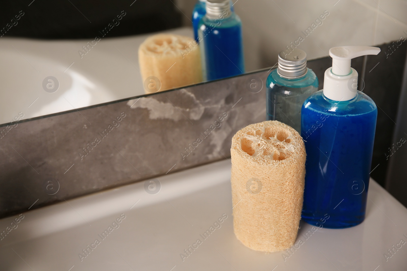 Photo of Natural loofah sponge and shower gel bottles on washbasin in bathroom