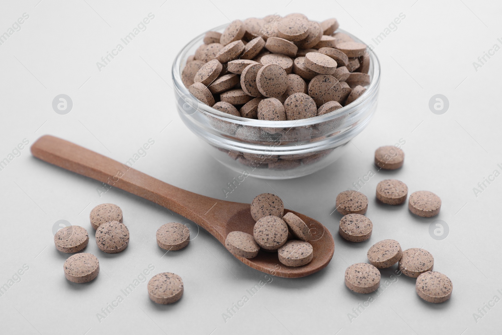 Photo of Glass bowl and wooden spoon with brewer`s yeast tablets on light grey background