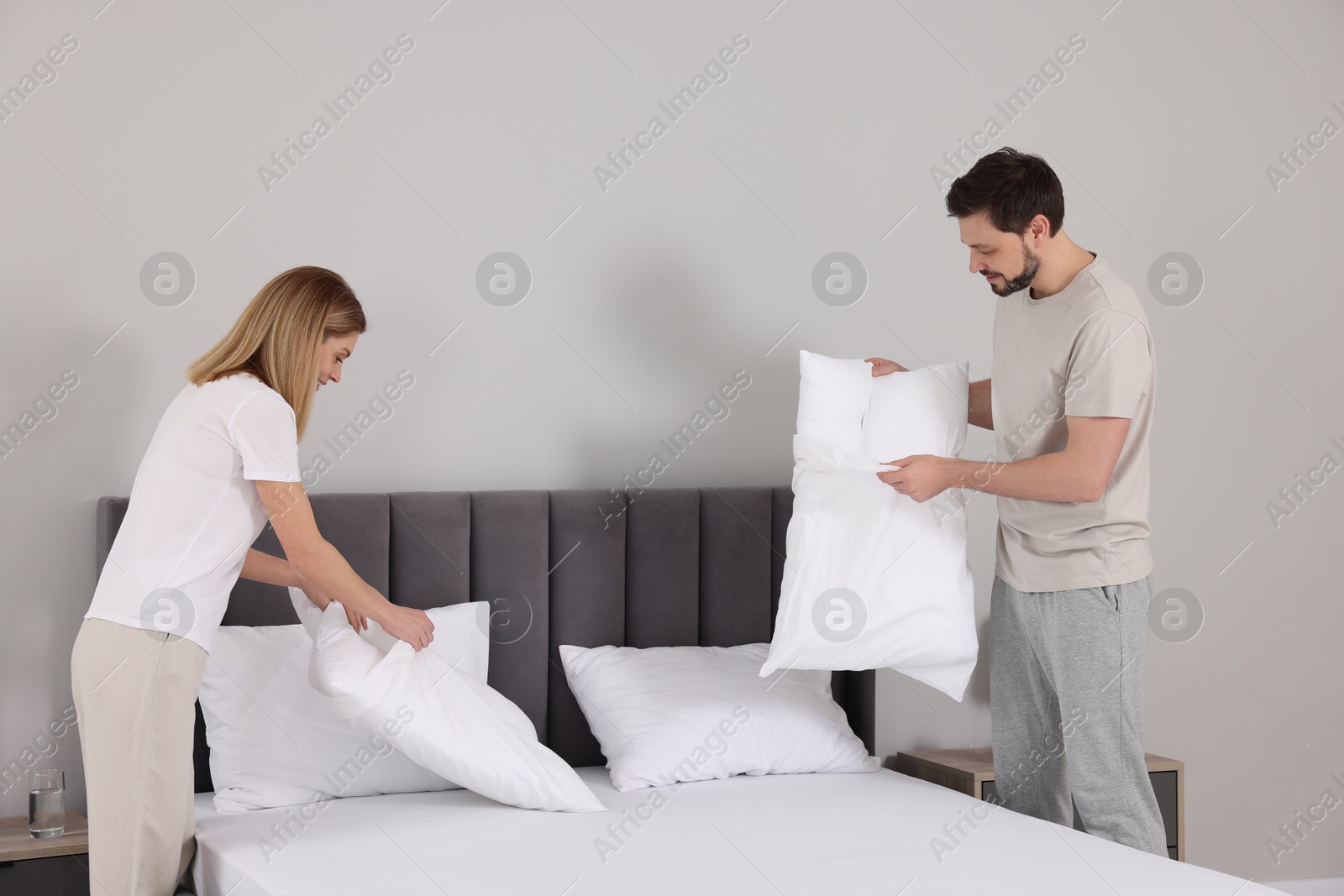 Photo of Couple changing bed linens in room. Domestic chores