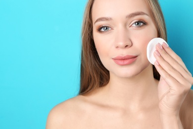 Photo of Portrait of beautiful young woman removing makeup with cotton pad on color background