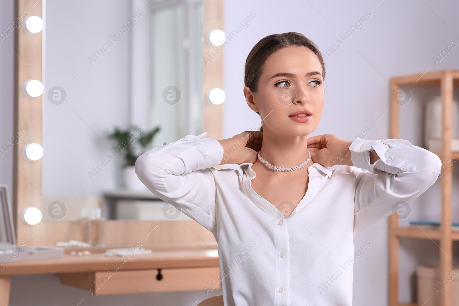 Photo of Young woman trying on elegant pearl necklace indoors, space for text