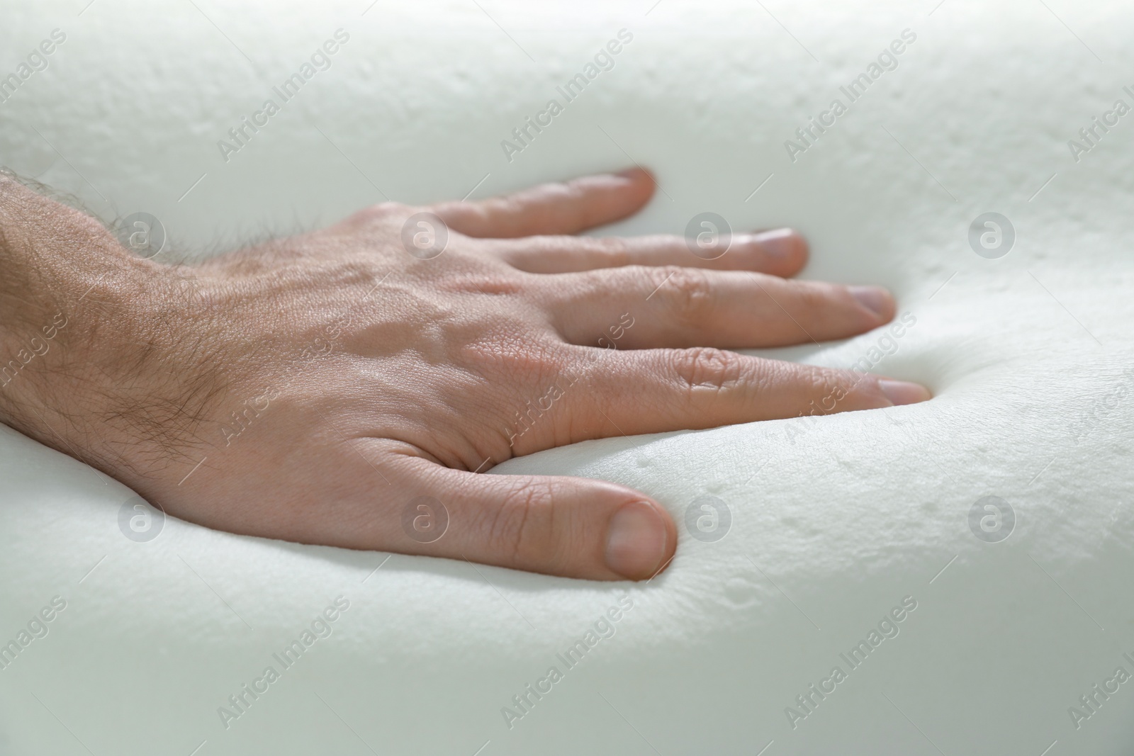 Photo of Man touching orthopedic memory foam pillow, closeup