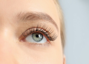 Young woman with beautiful long eyelashes on gray background, closeup. Extension procedure