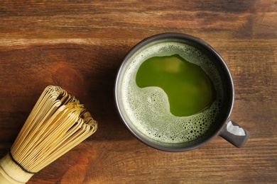 Photo of Cup of fresh matcha tea and chasen on wooden background, top view