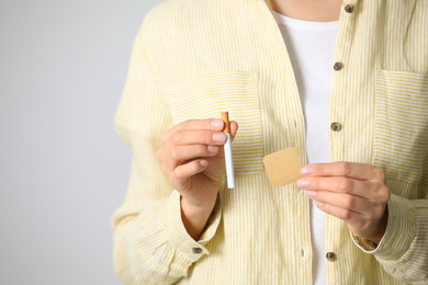 Photo of Young woman with nicotine patch and cigarette on light grey background, closeup