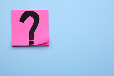 Sticky note with question mark on light blue background, top view. Space for text