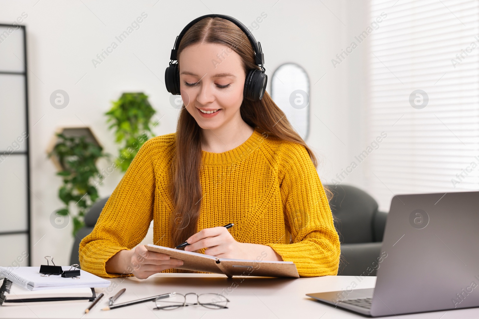 Photo of E-learning. Young woman taking notes during online lesson at white table indoors