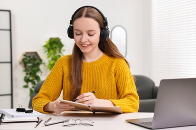 E-learning. Young woman taking notes during online lesson at white table indoors