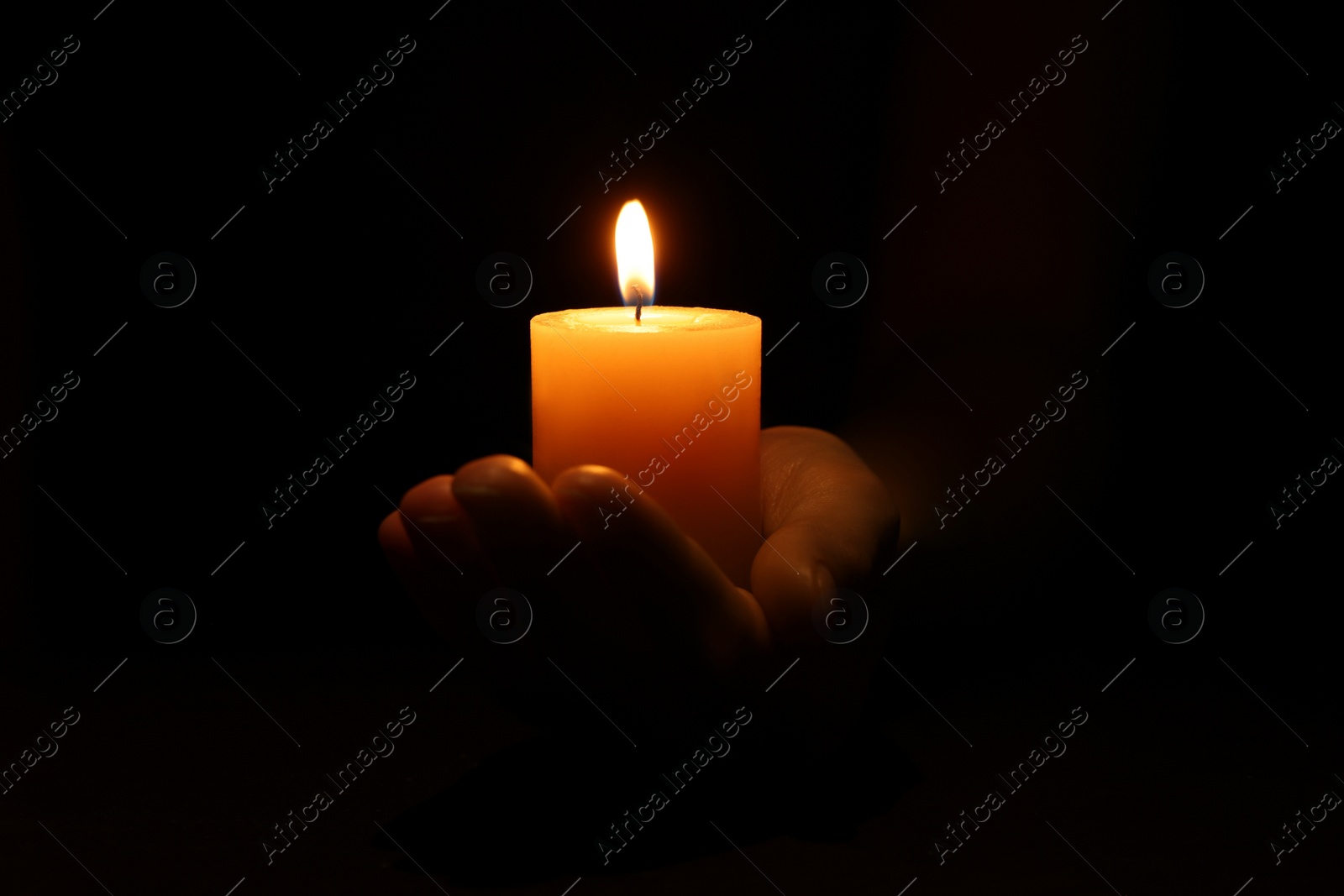 Photo of Woman holding burning candle in hand on black background, closeup