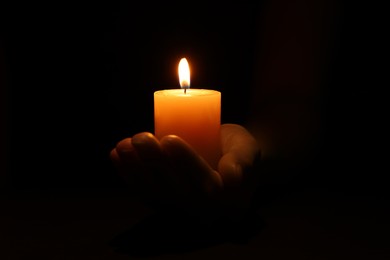 Woman holding burning candle in hand on black background, closeup