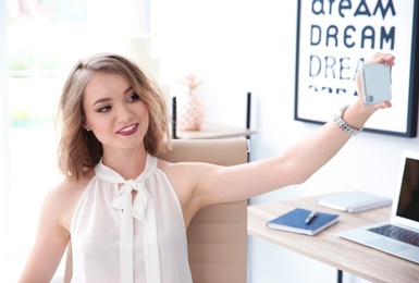 Photo of Beautiful young businesswoman taking selfie in office