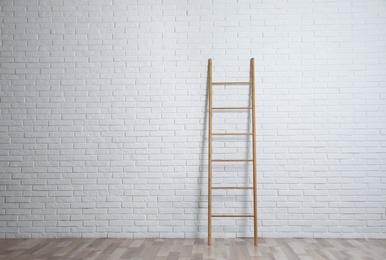 Photo of Modern wooden ladder near white brick wall