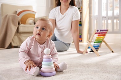 Cute baby girl playing with toy pyramid and mother on floor at home