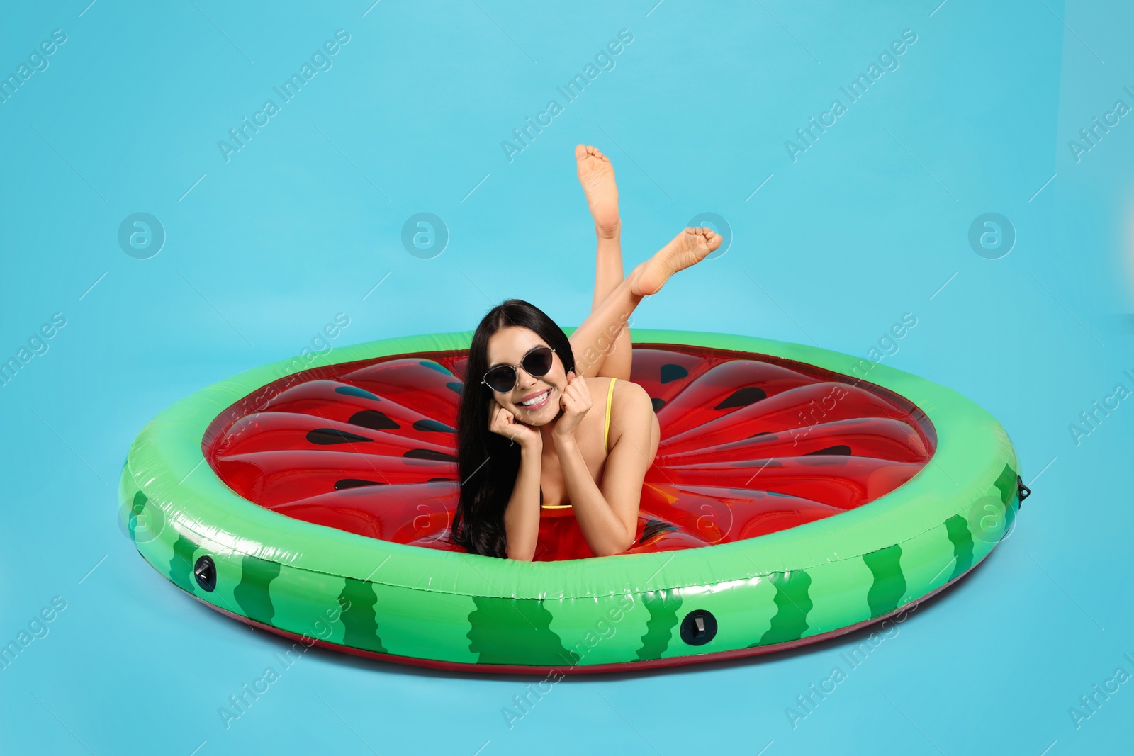 Photo of Young woman in stylish sunglasses on inflatable mattress against light blue background