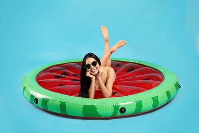 Photo of Young woman in stylish sunglasses on inflatable mattress against light blue background