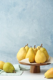 Stand with fresh ripe pears on table against color background