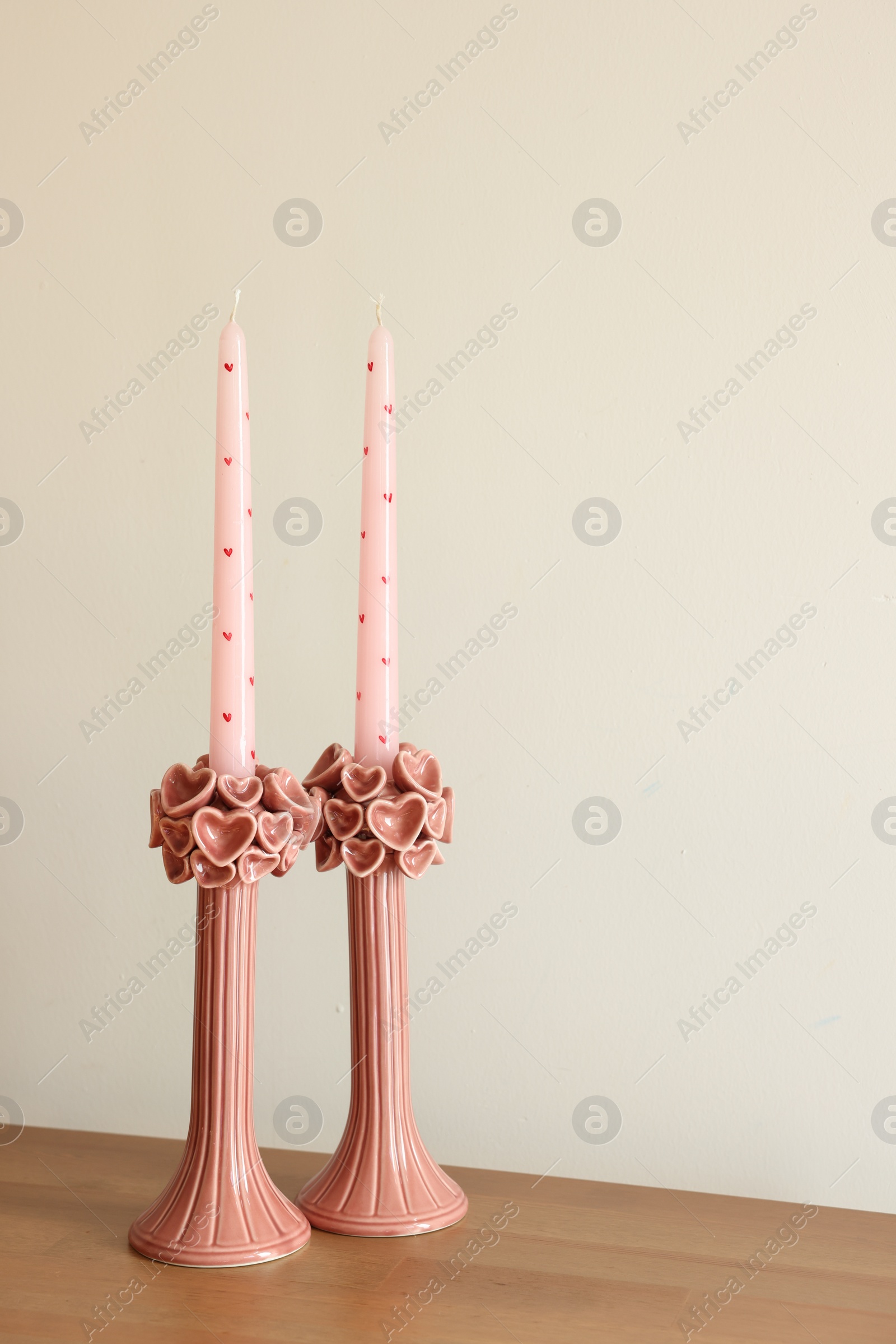 Photo of Beautiful pink wax candles on wooden table near white wall