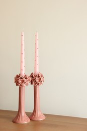 Beautiful pink wax candles on wooden table near white wall