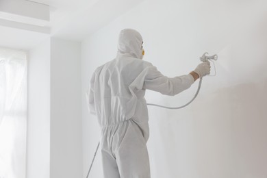 Decorator painting white wall with spray indoors, back view