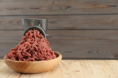 Photo of Mincing beef with manual meat grinder on wooden table, space for text