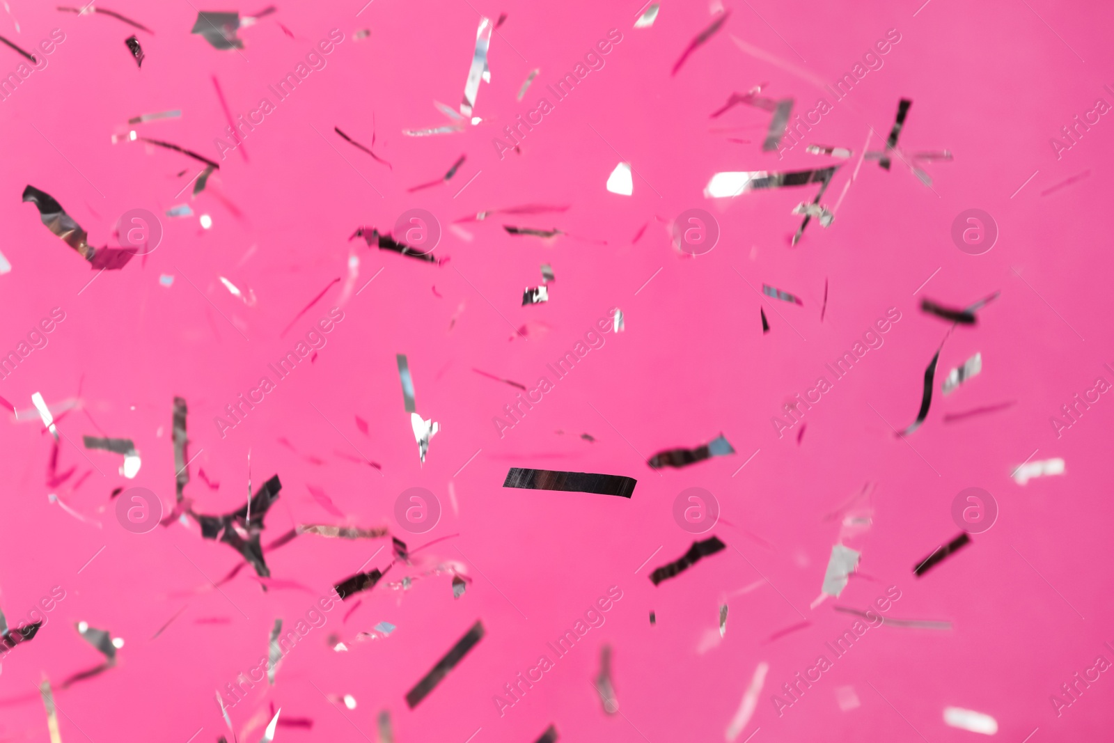 Photo of Shiny silver confetti falling down on pink background