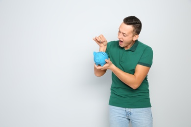 Photo of Young man putting coin into piggy bank on white background. Space for text