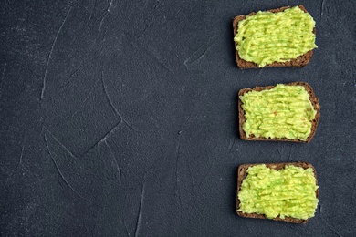Tasty crisp rye toasts with avocado on dark table, top view