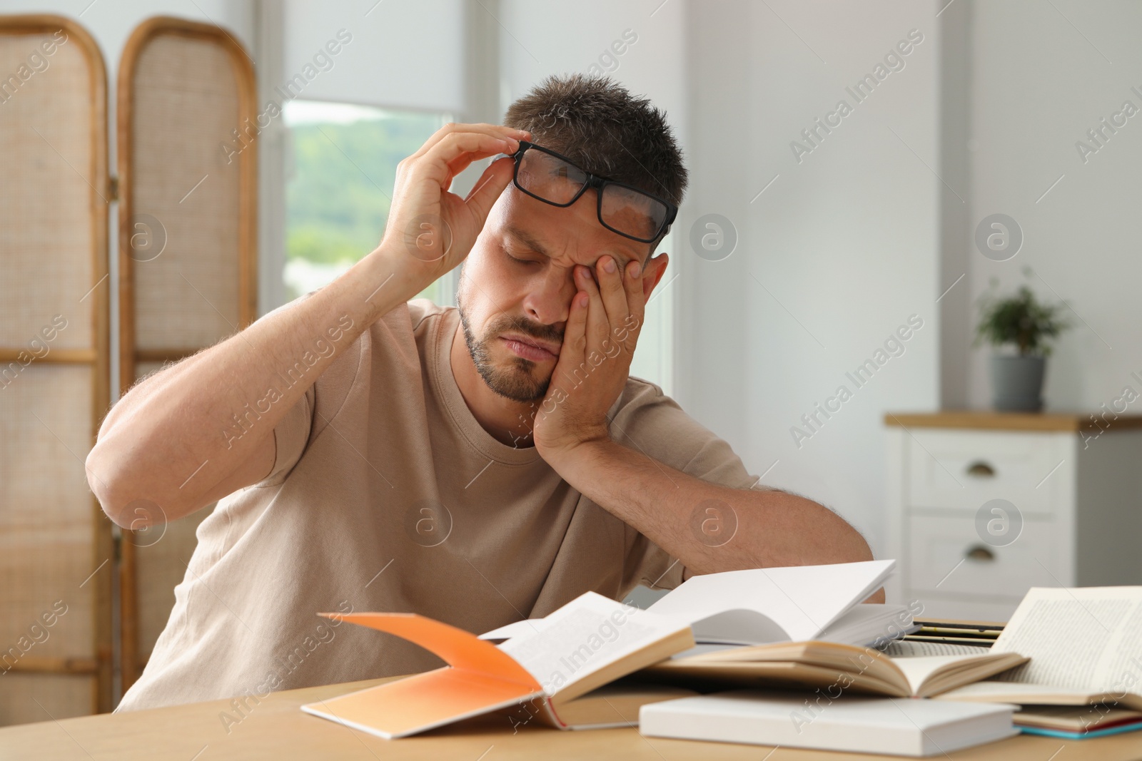 Photo of Sleepy man studying at wooden table indoors