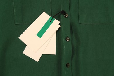 Blank white tags on green shirt, top view. Space for text