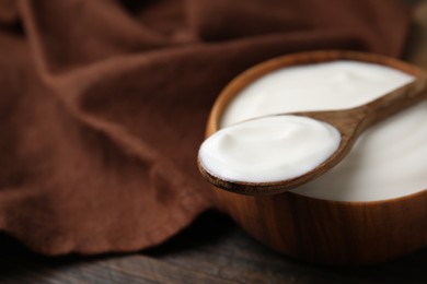 Delicious natural yogurt in bowl and spoon on wooden table, closeup. Space for text