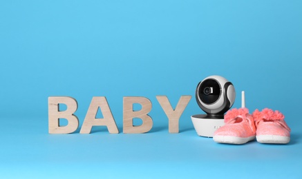 Modern CCTV security camera, small shoes and word BABY made of wooden letters on color background. Space for text