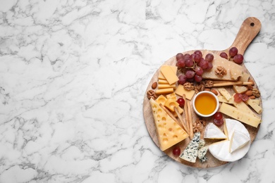Cheese plate with honey, grapes and nuts on white marble table, top view. Space for text