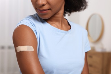 Photo of Young woman with adhesive bandage on her arm after vaccination indoors, closeup