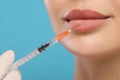 Doctor giving lips injection to young woman on light blue background, closeup. Cosmetic surgery