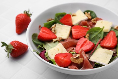 Photo of Tasty salad with brie cheese, prosciutto, strawberries and walnuts on white tiled table, closeup