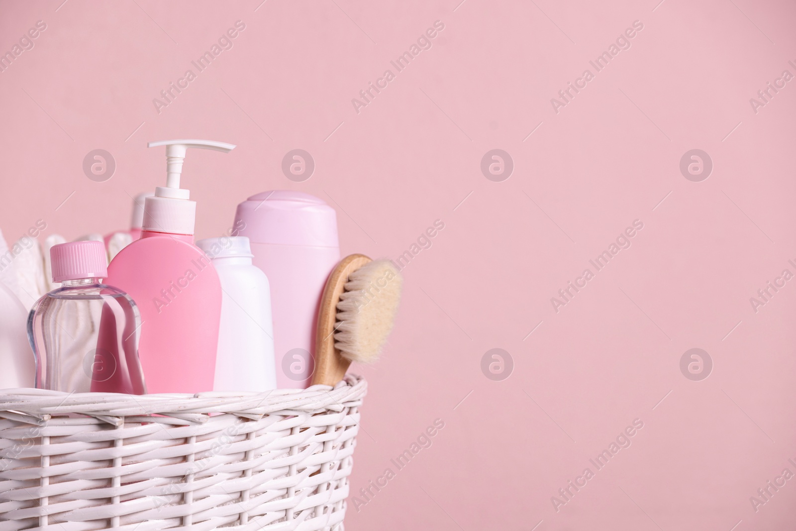 Photo of Baby cosmetic products in wicker basket on pink background. Space for text