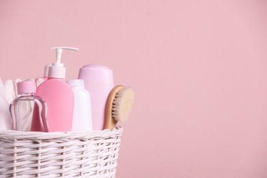 Photo of Baby cosmetic products in wicker basket on pink background. Space for text