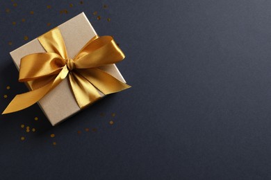 Photo of Beautiful golden gift box and confetti on black background, flat lay. Space for text
