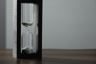 Photo of Hourglass with flowing sand on wooden table, space for text