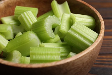 Photo of Fresh cut celery stalks in bowl on wooden table, closeup
