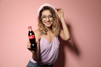 Photo of MYKOLAIV, UKRAINE - NOVEMBER 28, 2018: Young woman with bottle of Coca-Cola on color background