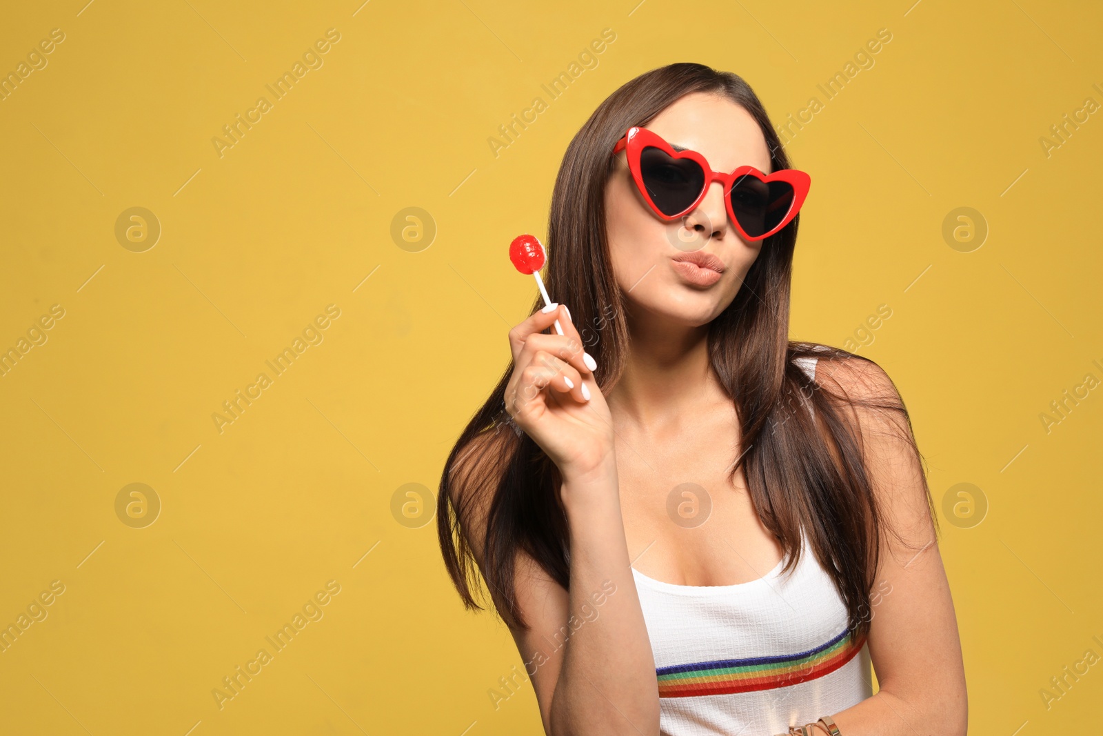 Photo of Portrait of beautiful young woman with heart shaped sunglasses and lollipop on color background. Space for text