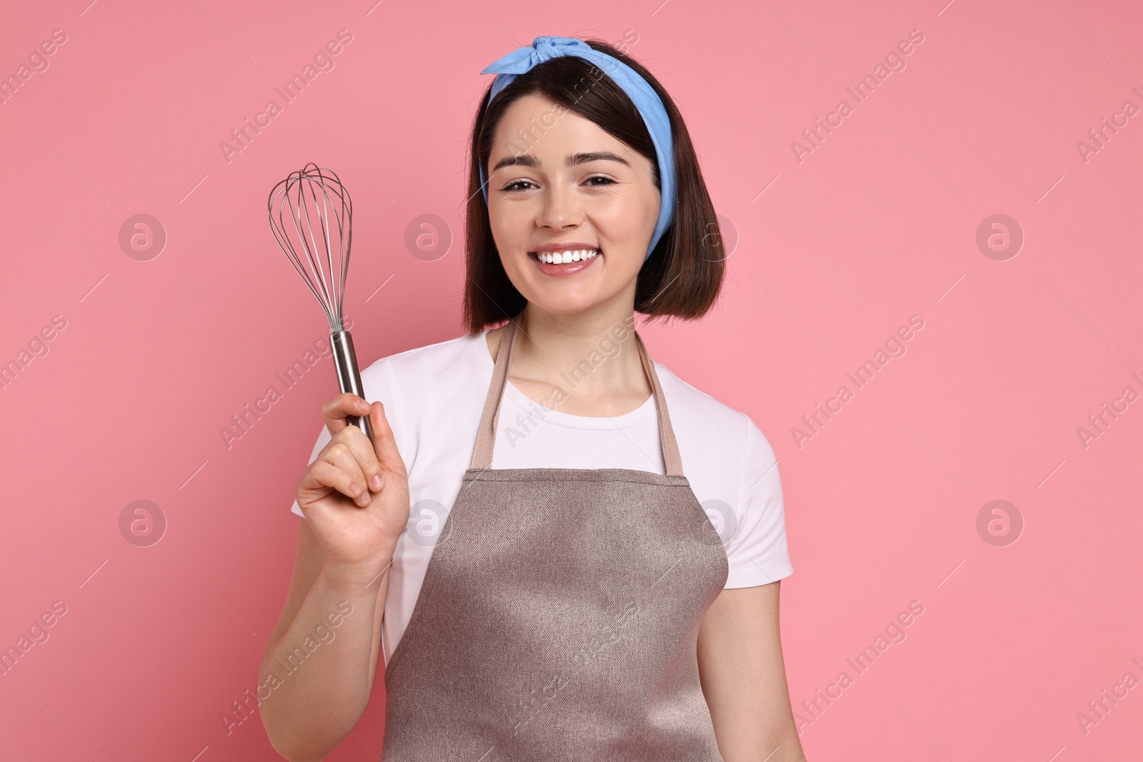 Photo of Happy confectioner with whisk on pink background