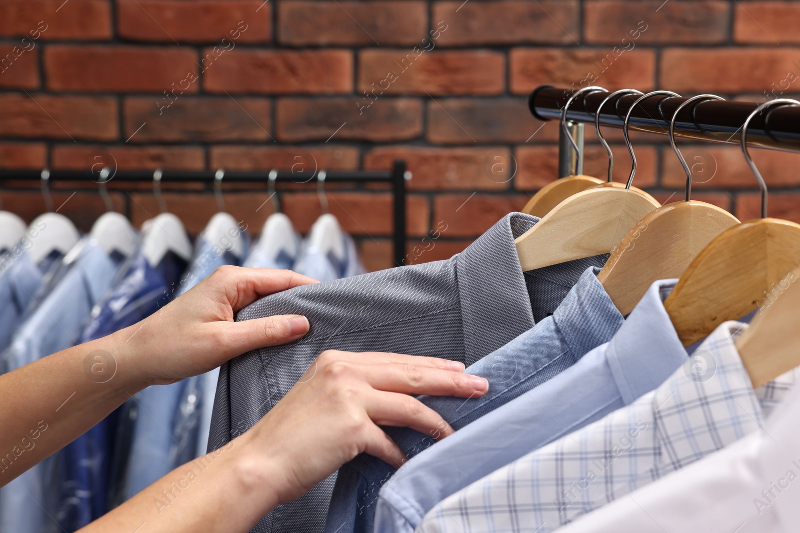 Photo of Dry-cleaning service. Woman taking shirt from rack against brick wall, closeup